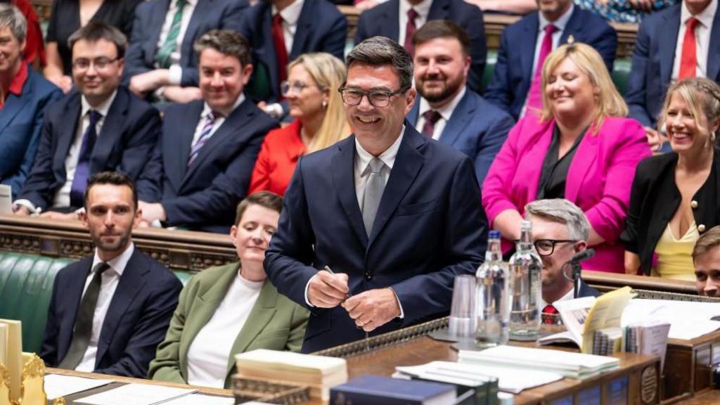 Andy Burnham is pictured laughing in parliament during his swearing-in ceremony, with Labour MPs on the benches behind him.