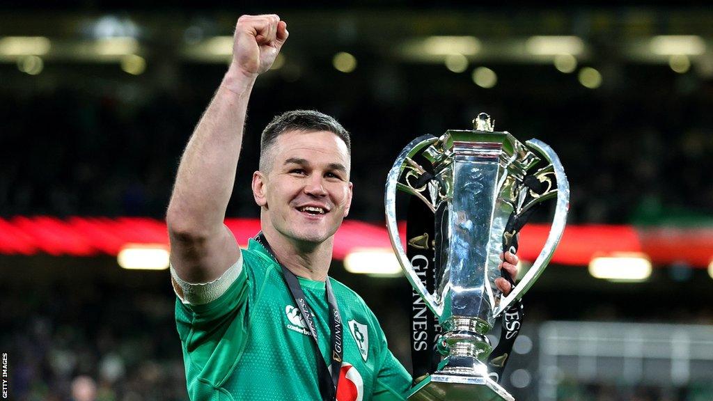 Ireland's Johnny Sexton raises one fist in the air to celebrate while holding the Six Nations trophy in his other hand