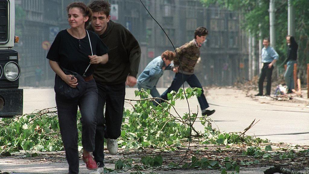 Sarajevo residents run through an intersection known for sniper activity after a shell fell in the center of the city on June 20, 1992