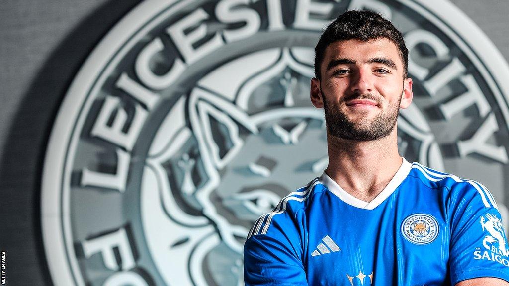 Tom Cannon with his arms folded in front of a giant Leicester City badge