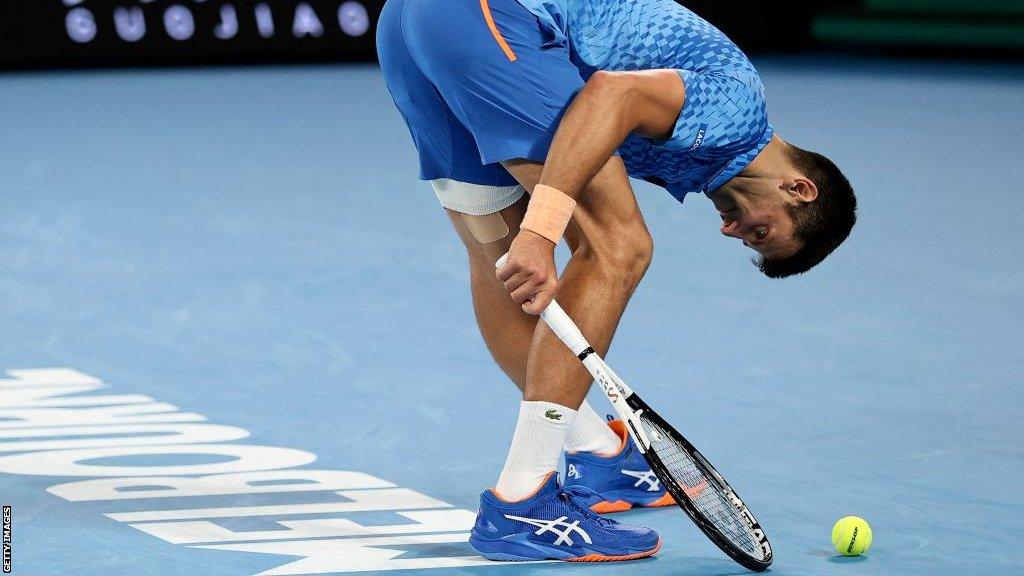 Novak Djokovic stretches out his left hamstring