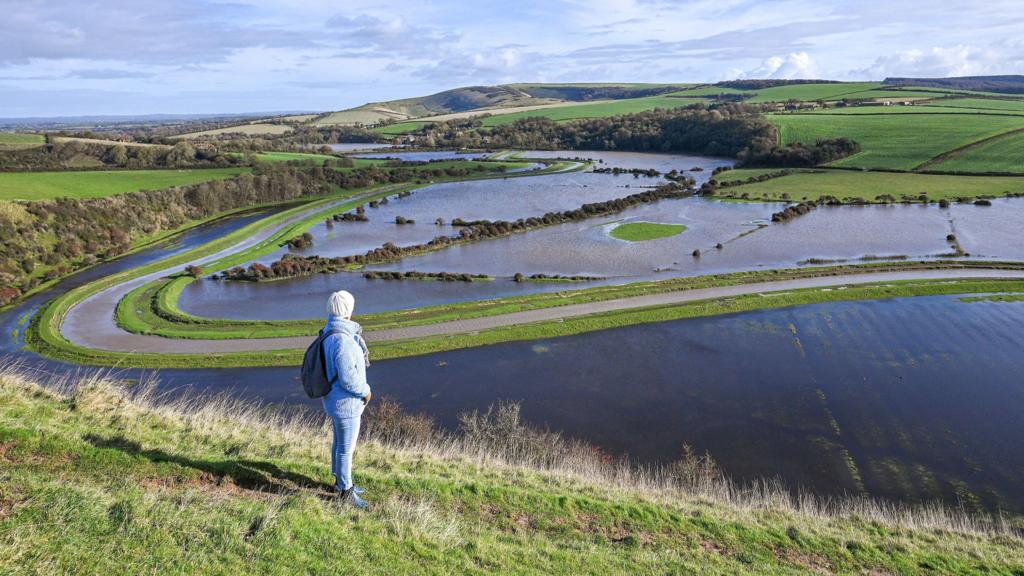 A walker looks out over flooded fields and farmland at Alfriston in East Sussex