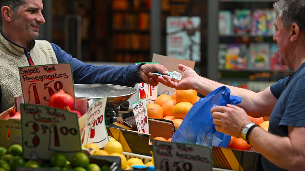A trader gives change to a customer at a market stall in London on 12 May 2022