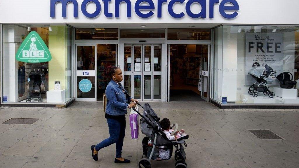 Woman with push chair walks past mothercare store