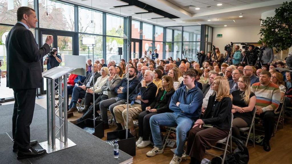 Rhun ap Iorwerth on stage addressing a seated audience