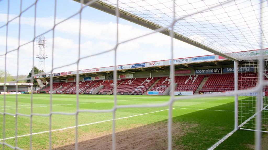 A view through the football net of Cheltenham Town FC's stadium, looking towards the red seats