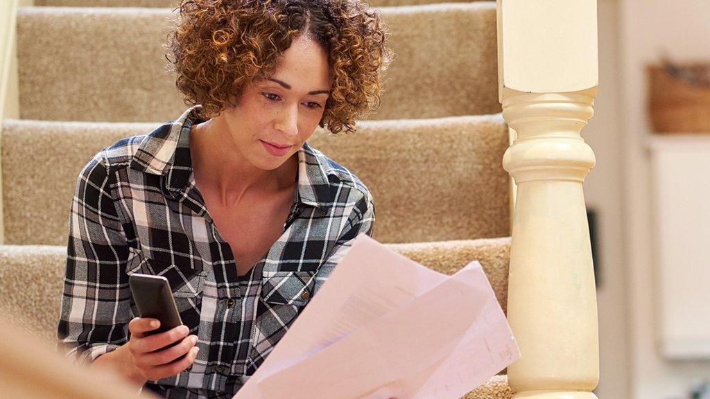 A woman sitting on the stairs holding a phone and some bills