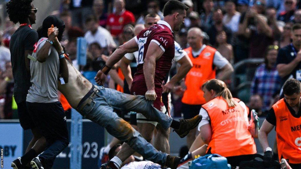 A Just Stop Oil protestor is escorted off the pitch after disrupting the Gallagher Premiership final between Saracens and Sale at Twickenham