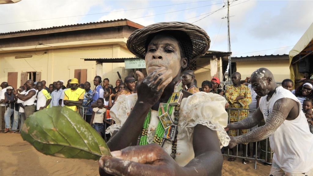 A man dressed as a woman uses a leaf to look at himself on November 1, 2011 on Abissa square