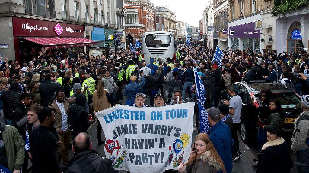 Fans in a busy street holding a sign saying Jamie Vardy's havin' a party