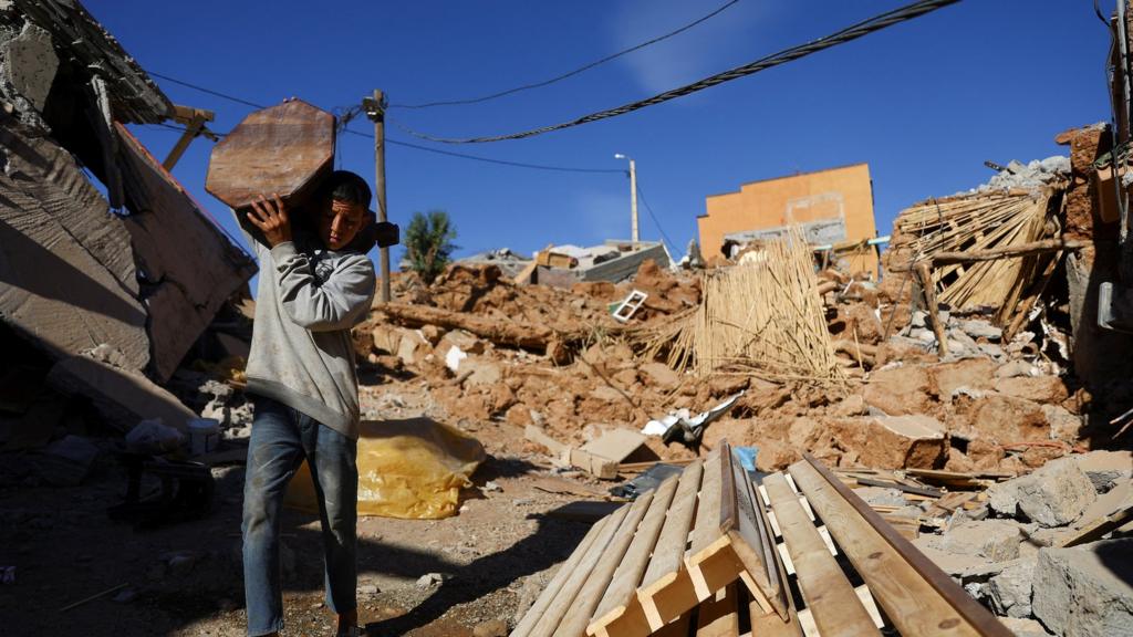 Boy carrying item of furniture amod rubble in Talat N'Yaaqoub. Morocco