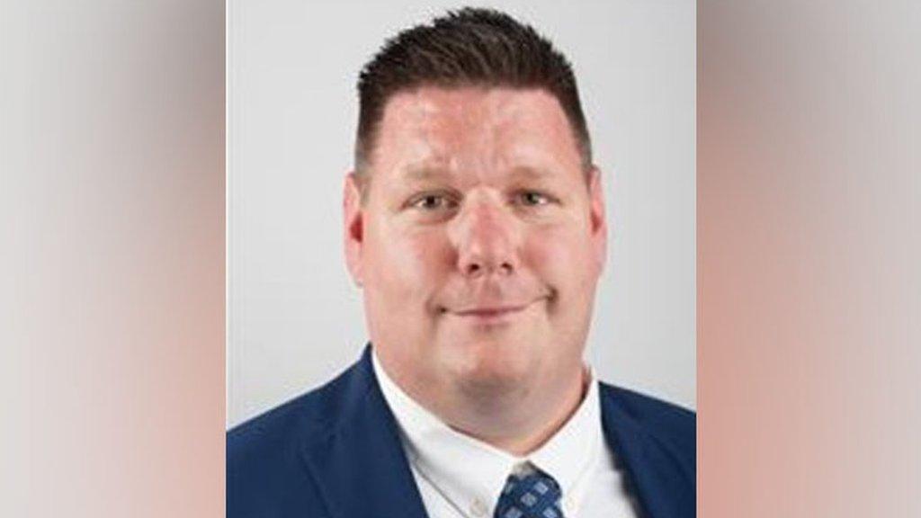 A thick- set man in a blue suit and blue tie with spots on it