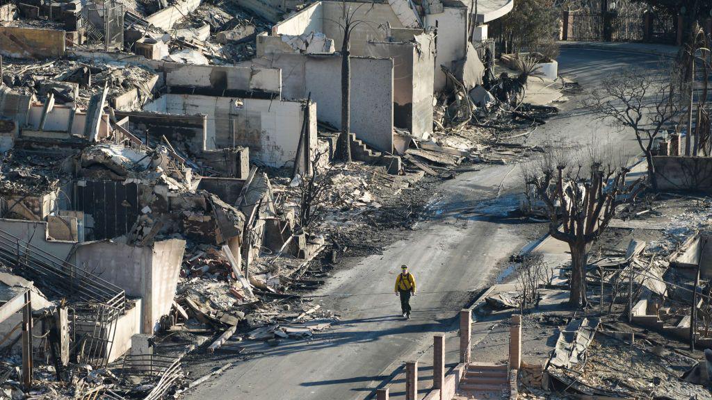 A person walks through a street of houses destroyed by fires