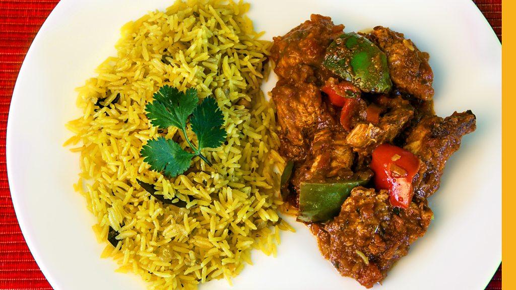 A plate of yellow pilau rice on the left and chicken curry on the right on a white plate.