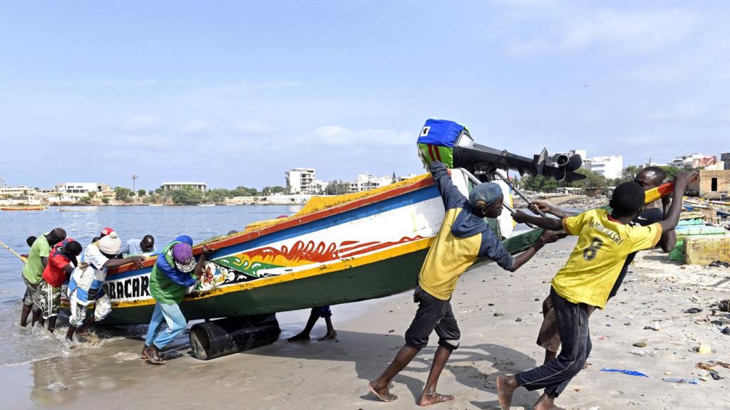 Young fishermen pull a wooden pirogue to the shore of the traditional fishing harbour of Soumbedioune in Dakar, on July 2, 2015.