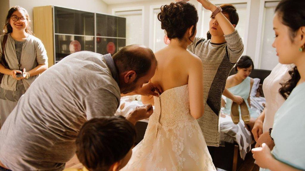 Syrian refugee Ibrahim Halil Dudu fixes the broken zip on Jo Du's wedding dress watched by bridesmaids