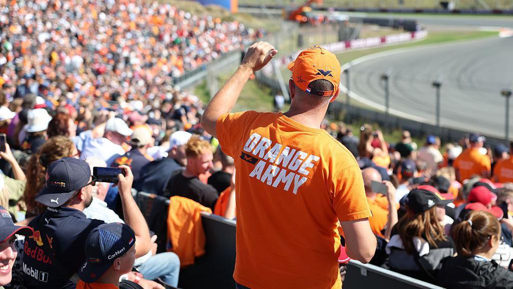 A fan in an orange army t-shirt stands in the grandstands at Zandvoort 