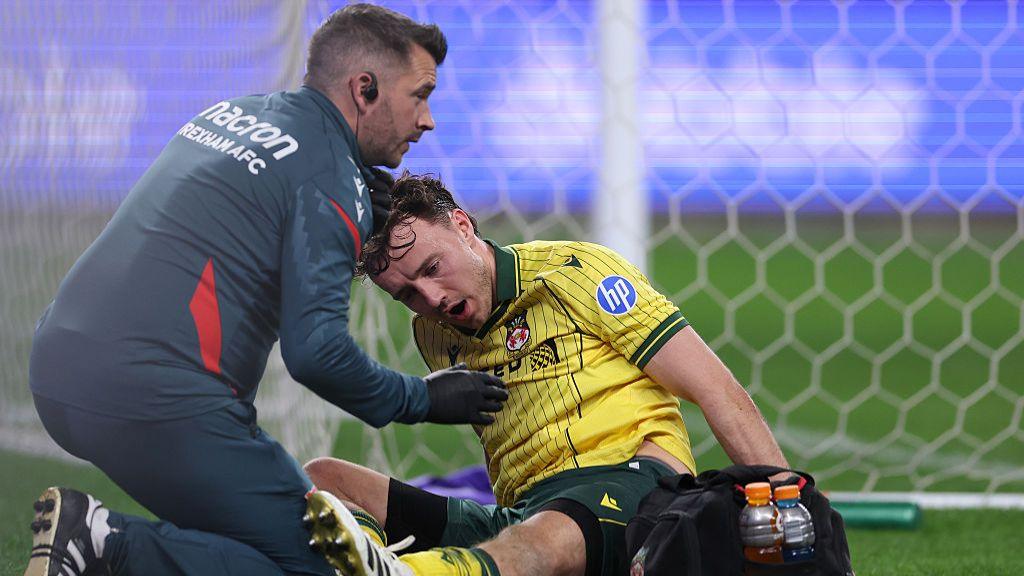 Wrexham's Ollie Rathbone (right) receives treatment