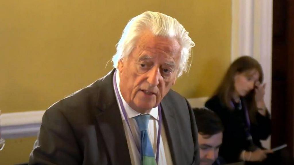 Michael Mansfield addressing the inquiry. He is wearing a dark grey suit, blue and green tie, and has long white hair pushed back.