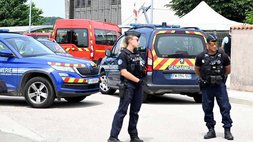 Gendarmes stand before police vehicles at the scene of the fatal stabbing in Nogent
