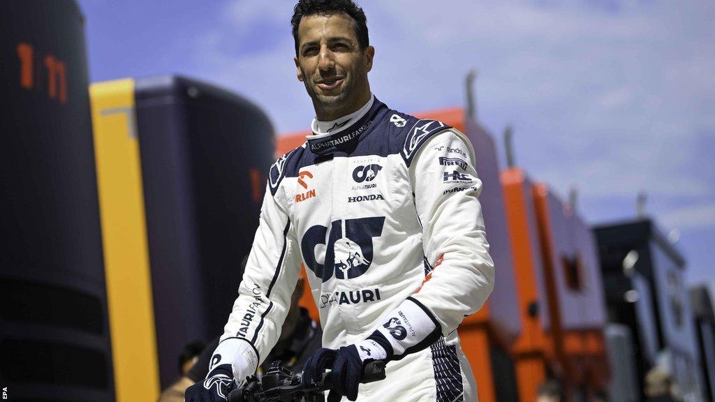 Alpha Tauri driver Daniel Ricciardo smiles as he rides a scooter through the paddock at the Hungarian Grand Prix