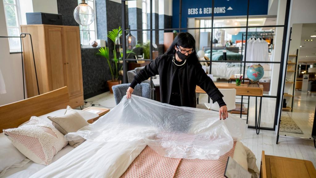 A member of staff wearing PPE (personal protective equipment), including a face mask as a precautionary measure against COVID-19, demonstrates the use of plastic film for customers to test beds, at the re-opened Heal's flagship store in central London on June 8, 2020