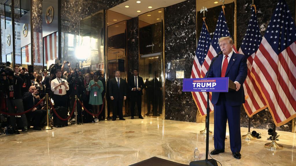 Donald Trump speaking in front of US flag with audience in background