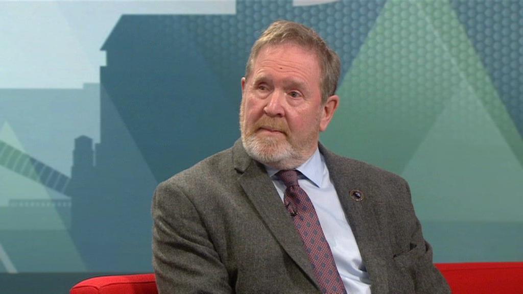 Anti-knife crime campaigner Mark Brindley sits on a red sofa with a blue backdrop behind him. He looks to the left of the camera with a solemn expression. He is wearing a grey suit jacket, light shirt and a dark patterned tie.