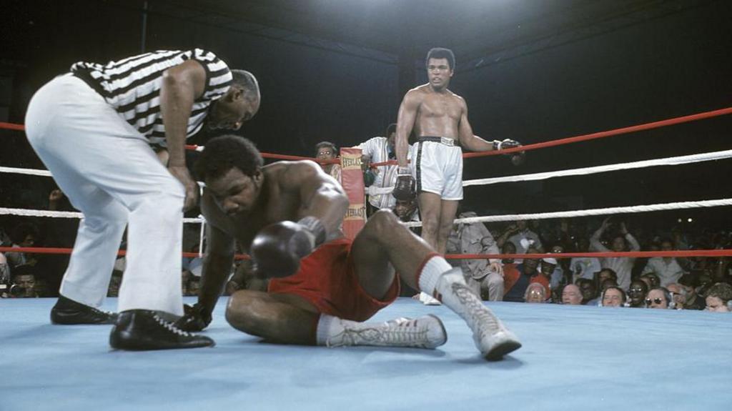 George Foreman tries to get off the canvas with Muhammd Ali in the background