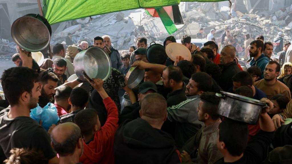 Displaced Palestinians hold out pots to get food