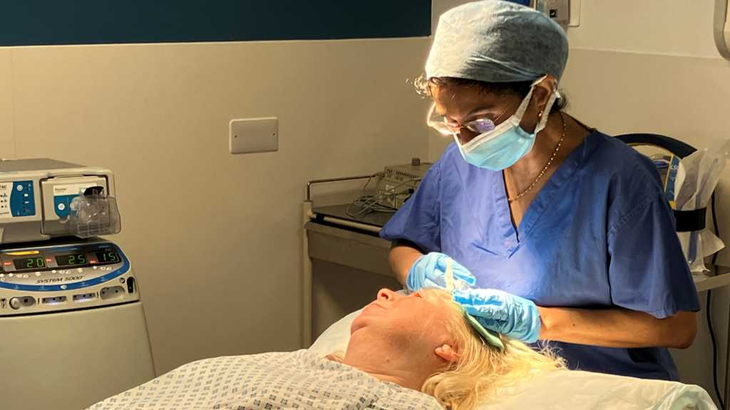 A picture in the operating theatre at Newark Hospital where the consultant dermatologist wearing surgical clothing is carrying out a procedure to remove a skin cancer lesion. Fiona Hayward Lyon is lying down on the theatre trolley. 