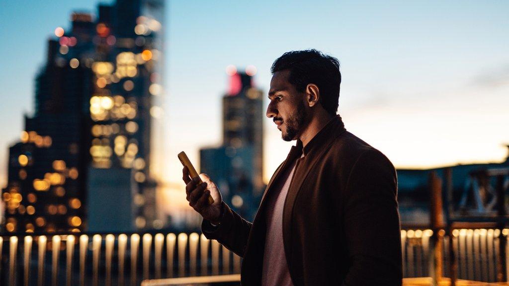 Businessman using his phone on roof with London skyline in background