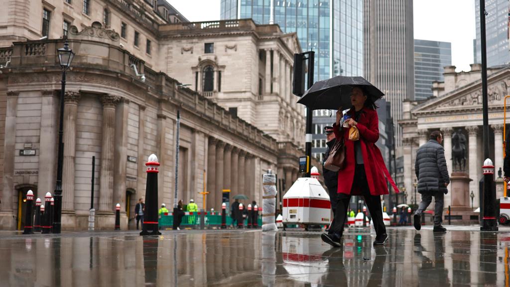 A pedestrian with an umbrella walks by the Bank of England building and Stock Exchange building, in the financial district, central London, on 2 November 2023