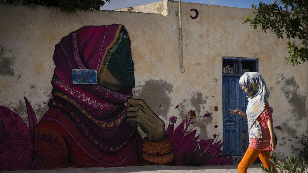 A woman walks past a mural by Mexican artist SANER in the village of Erriadh, on the Tunisian island of Djerba.