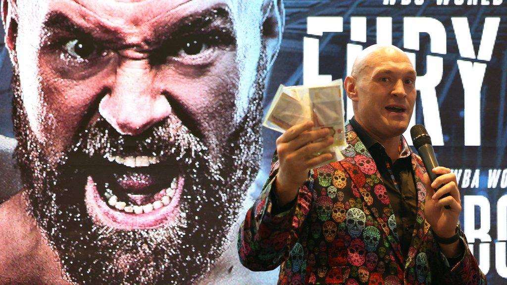 Tyson Fury stands with a wad of cash in his hand