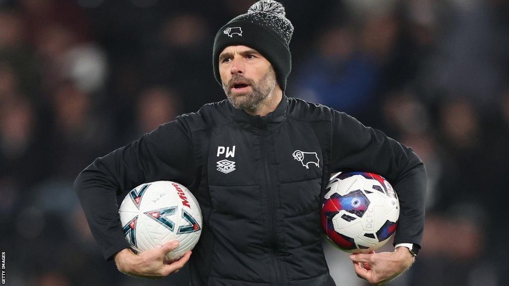 Paul Warne watching his Derby team warm up while holding footballs under his arms