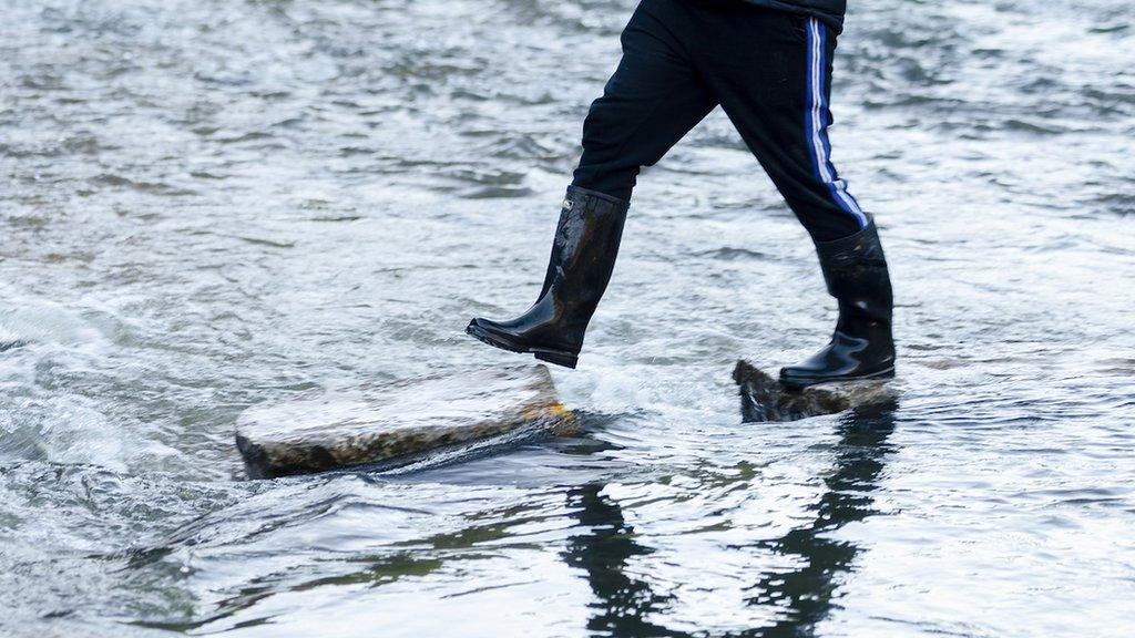 A man carrying a dog steps cautiously over the dislodged stones on 24 November 2023