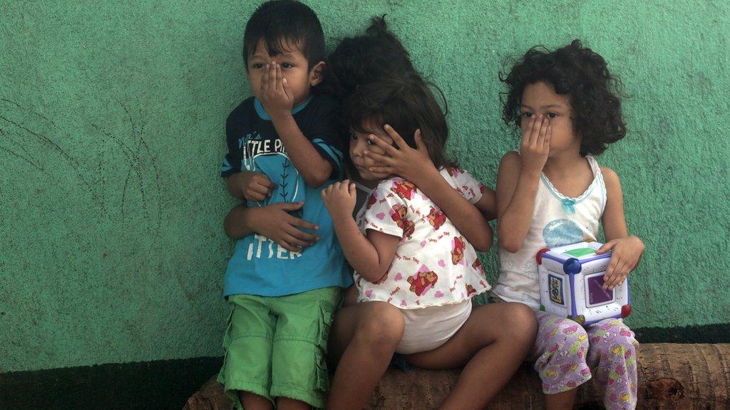 Children cover their faces outside their house while a health ministry worker fumigates to kill mosquitoes