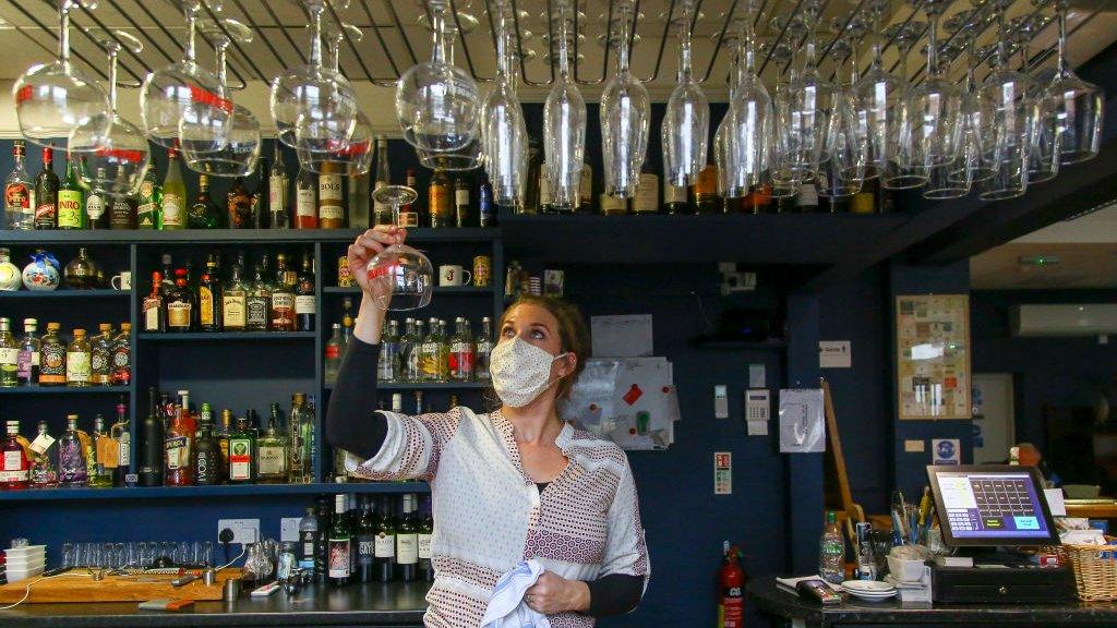 A woman behind a bar wipes glasses