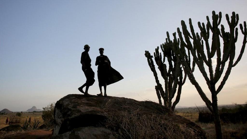 Two men standing on a rock. It is getting dark. You can just see their silhouettes.