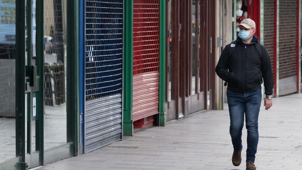 man in mask walking past closed shops