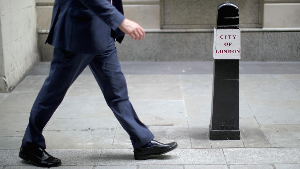 A man walking on a street next to a City of London bollard