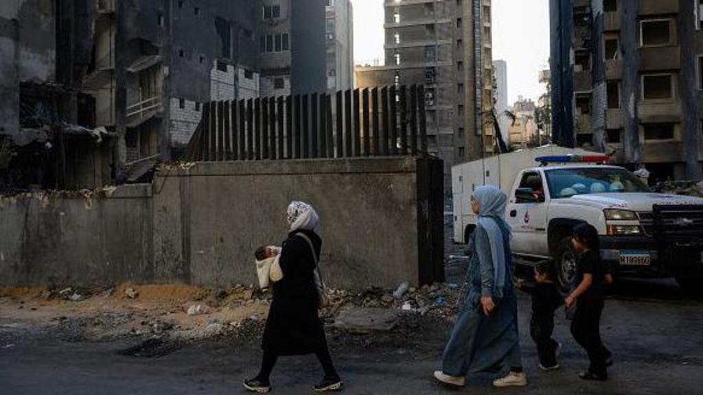 A woman carrying a baby walks past destroyed buildings n Lebanon.