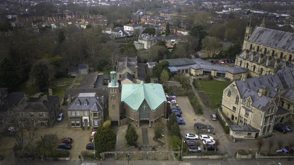 A drone image looks down on a cathedral and a church with houses and trees behind them.