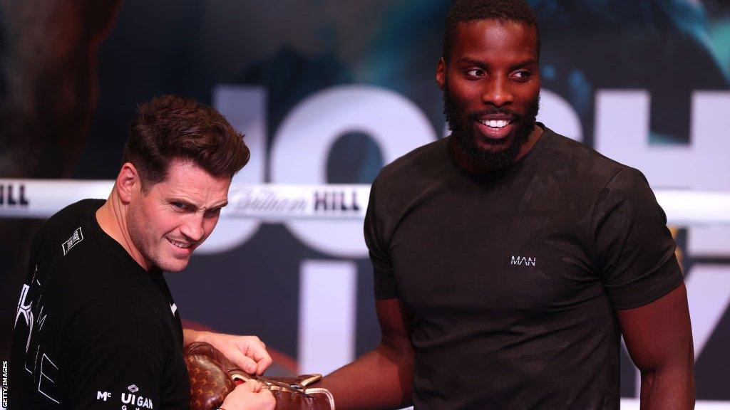 Shane McGuigan putting boxing gloves on Lawrence Okolie