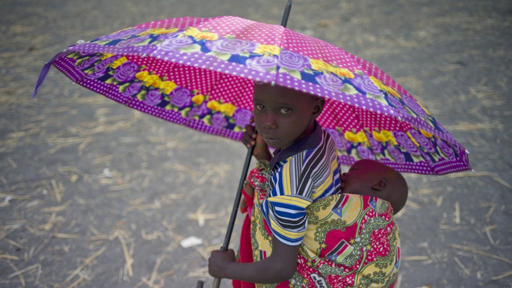 A refugee child from South Sudan with a baby on her back holding an umbrella in Uganda - 2017