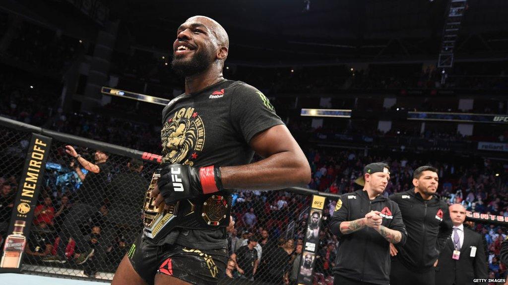 Jon Jones smiles with the UFC light-heavyweight belt around his waist in the cage