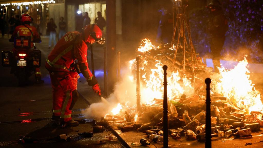 A firefighter uses a fire extinguisher on a burning pile of bottles