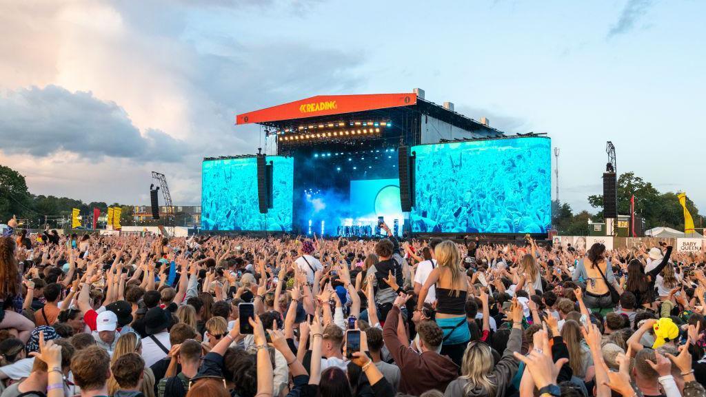 Revellers enjoying the main stage of the festival in Reading in August 2023. The stage has two large screens to the left and the right of it. The stage and the screens are light blue