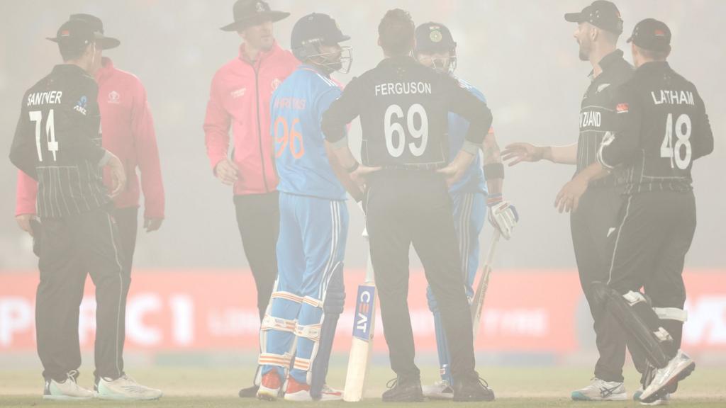 Players and umpires discuss as fog descends over the stadium